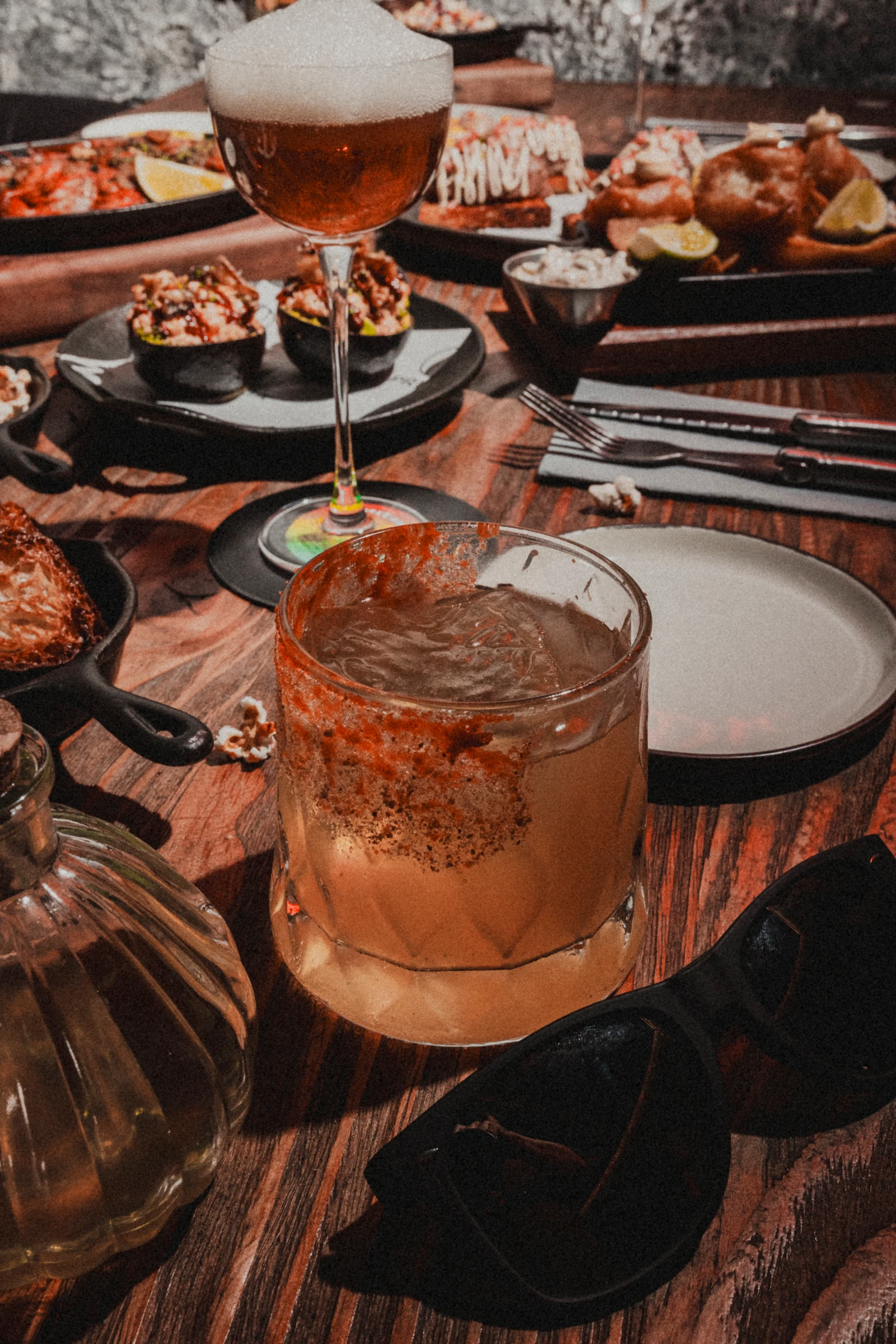 Cóctel con hielo y borde especiado junto a los platos de Prima